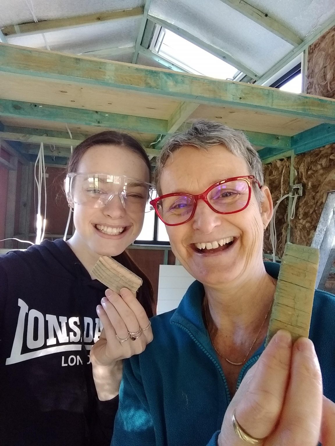 Malou and Anne-Marijke in their tiny house holding up pieces of timber