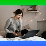 young woman sitting on bed looking at laptop