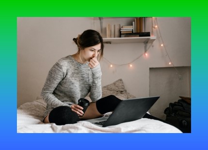 young woman sitting on bed looking at laptop